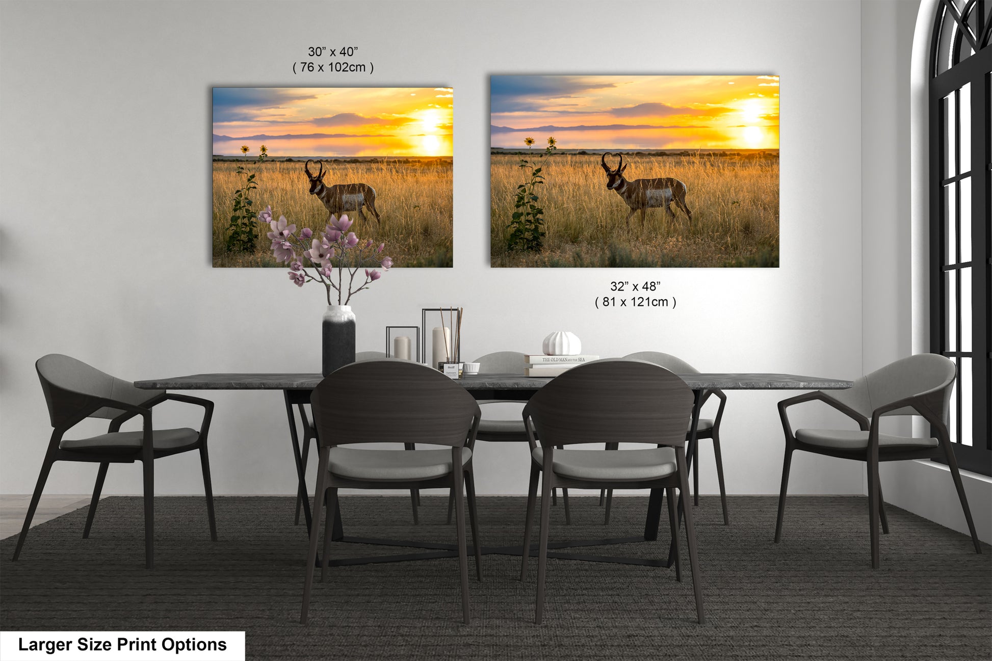a dining room with a large dining table and chairs. There are two framed prints of a sunset landscape hanging on the wall above the table.