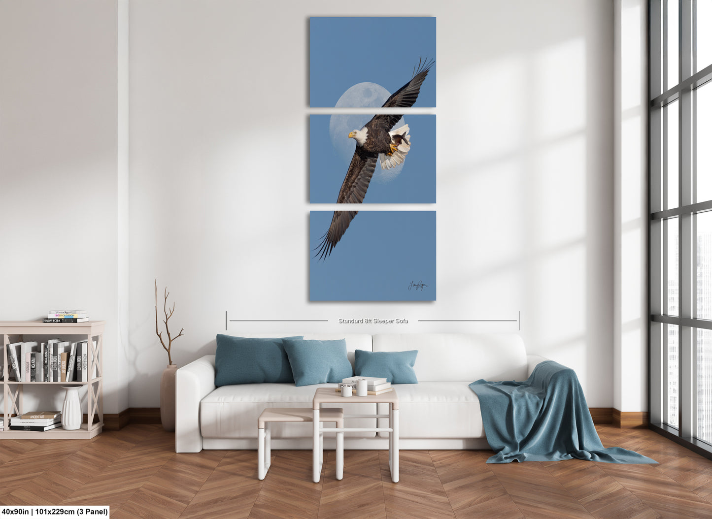 A modern living room with a white sofa, a coffee table, and a bookshelf. Above the sofa is a large blue and white bird painting depicting an eagle in flight.