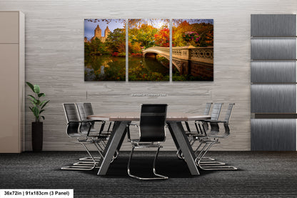 A modern office space with a large, three-panel landscape painting of Central Park in New York City hanging on the wall. The painting depicts the park's iconic landmarks and foliage during autumn. The office features a wooden table surrounded by black chairs, creating a professional and comfortable atmosphere.
