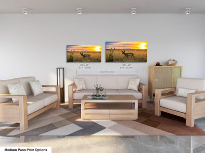 a living room with a sofa, two chairs, and a coffee table. There are two framed landscape paintings on the wall, one depicting a deer in a field and the other showing a sunset. The sofa and chairs are made of wood, and the coffee table is made of wood. The room has a neutral color scheme with a geometric patterned rug on the floor.