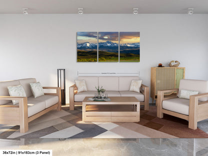 A modern living room with a large, three-panel landscape painting hanging on the wall. The painting depicts a scenic mountain range with a colorful sky. The room is furnished with a sofa, two armchairs, and a coffee table, creating a comfortable and inviting atmosphere.