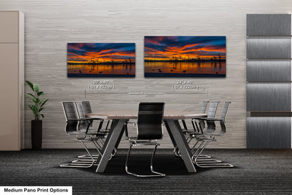 a modern office space with a large wall-mounted painting depicting a sunset over a city skyline. The painting is framed in a standard size of 24x48 inches and is displayed in two different positions on the wall. The office space includes a large conference table surrounded by chairs, creating a professional and comfortable environment for meetings and discussions.