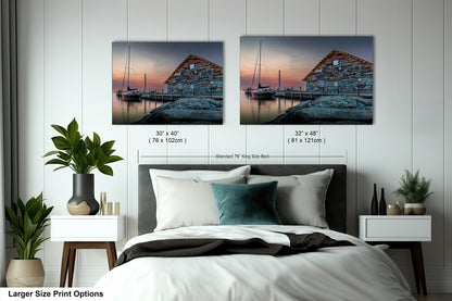 a bedroom with a large bed and two framed pictures of a building with a dock and a sailboat on the water. The pictures are hung on the wall above the bed, and there are two different sizes of the pictures, one larger and one smaller.