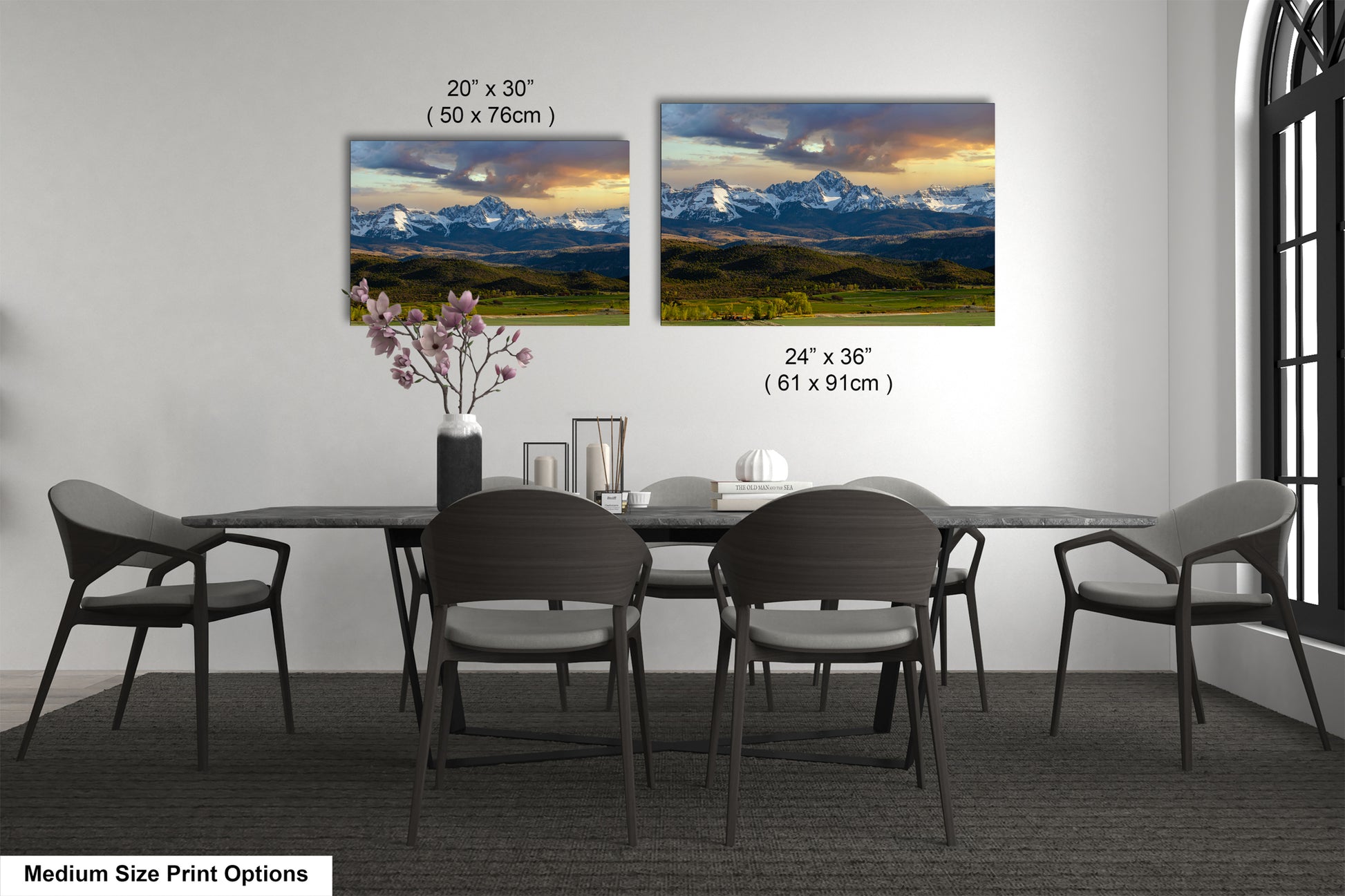 a dining room with a large dining table surrounded by six chairs. There are two framed landscape paintings hanging on the wall above the table, depicting a scenic mountain landscape. The paintings are of medium size, with dimensions of 20' x 30' (50 x 76') and 24' x 36' (61 x 91') respectively.