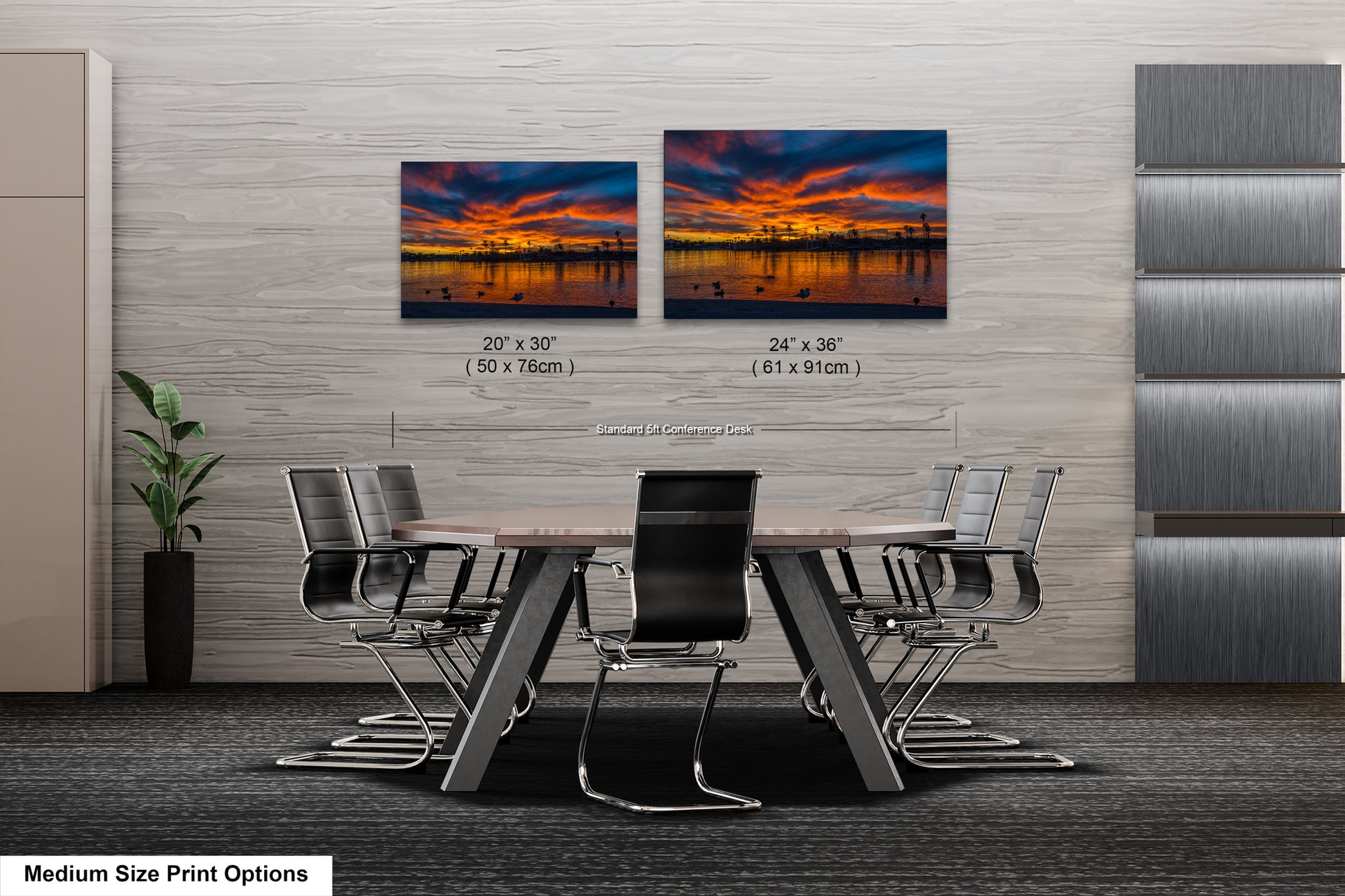 a modern office space with a large wooden table surrounded by black chairs. Two framed landscape photographs are displayed on the wall above the table, depicting a sunset over a body of water. The photographs are of medium size, with dimensions of 20 x 30" and 24 x 36" (61 x 91 mm").