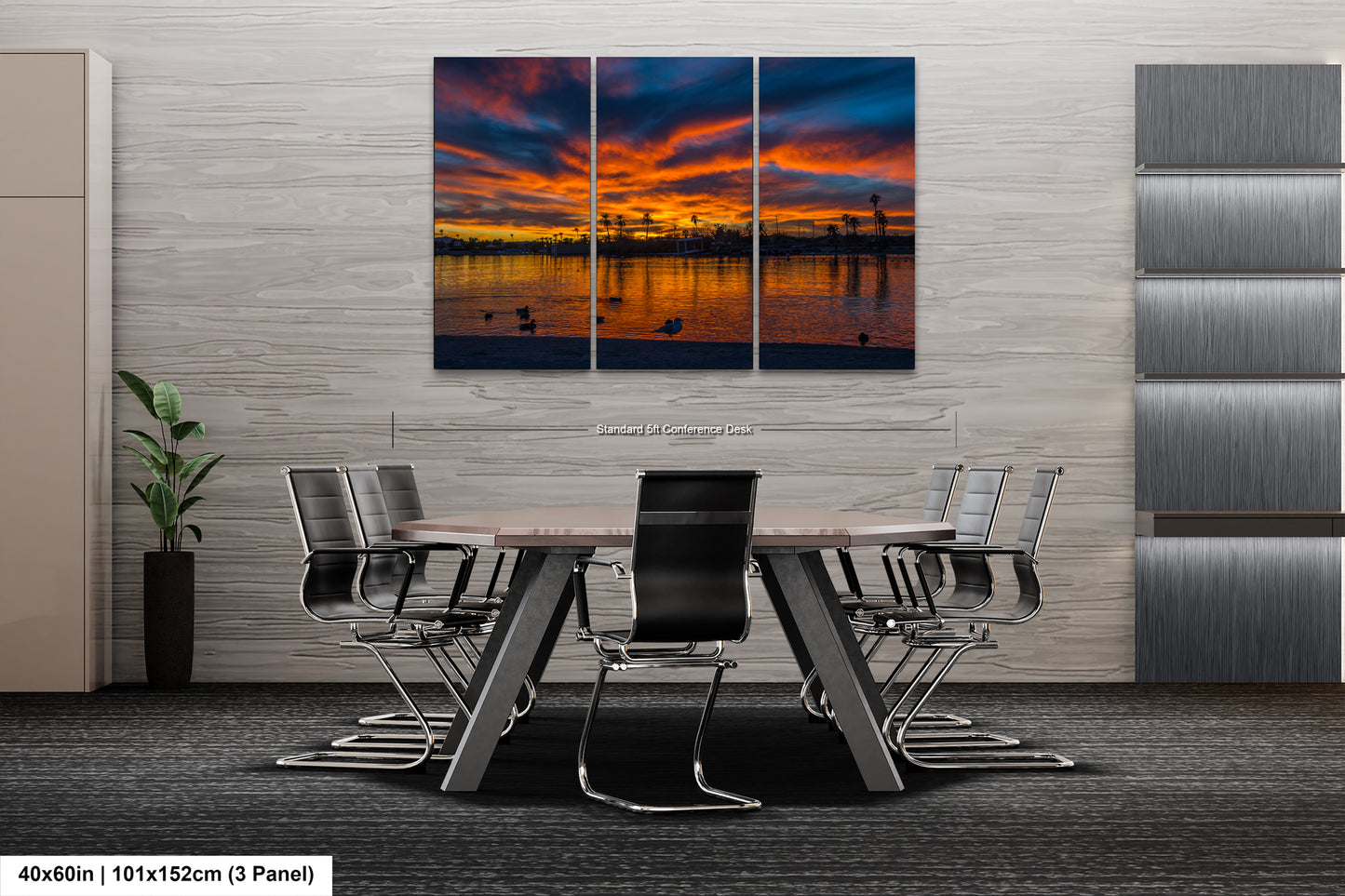 a modern office space with a large, three-panel landscape painting of a sunset over a body of water. The painting is displayed on the wall above a conference table with chairs arranged around it. The office has a minimalist and contemporary design, with gray walls and a gray carpet floor.
