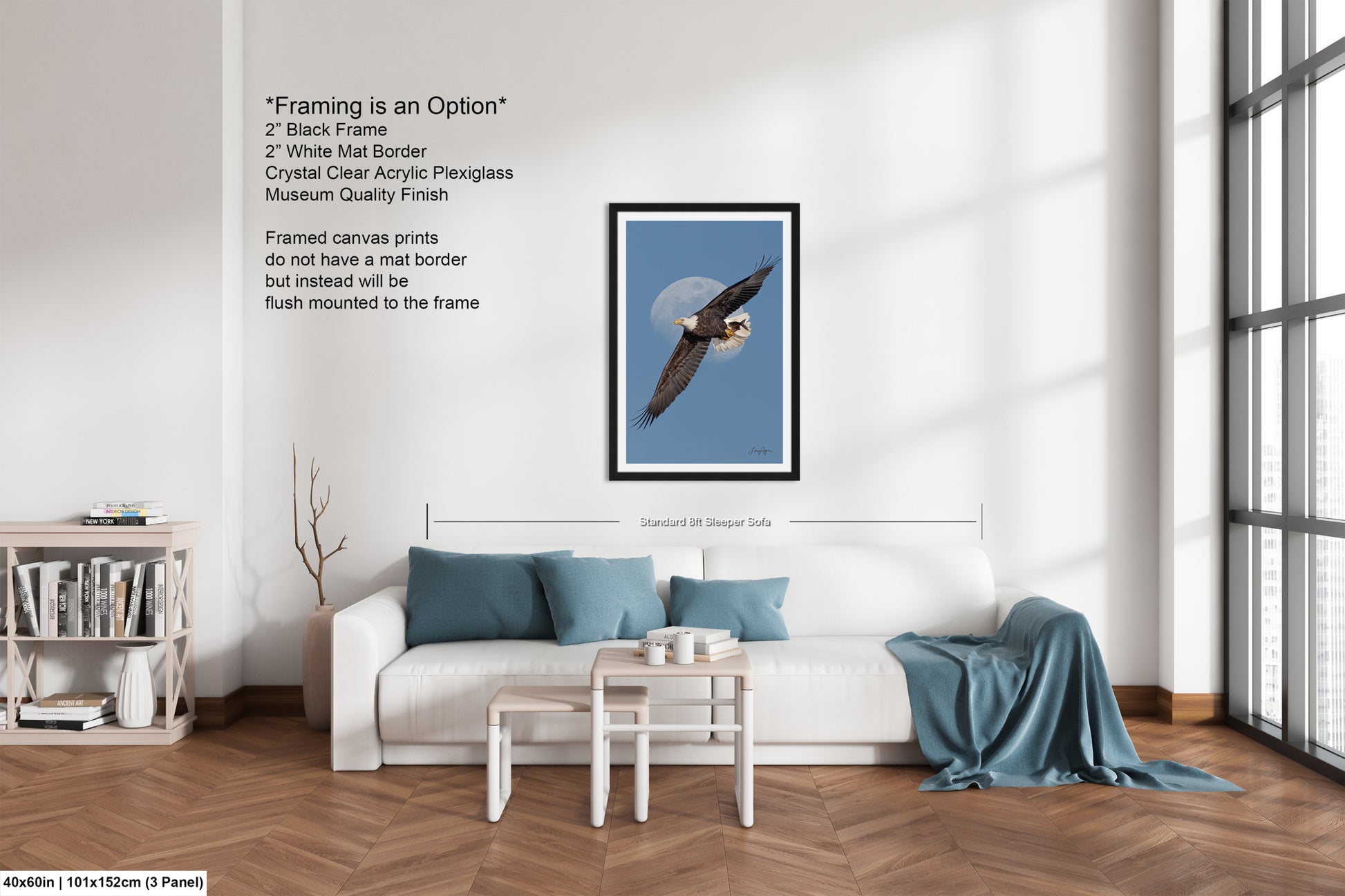 The image is a modern living room with a white sofa, a coffee table, and a bookshelf. There is a framed picture of a bald eagle on the wall, and a window with white blinds. The room has a minimalist and clean design, with a focus on the white furniture and the large window providing natural light.