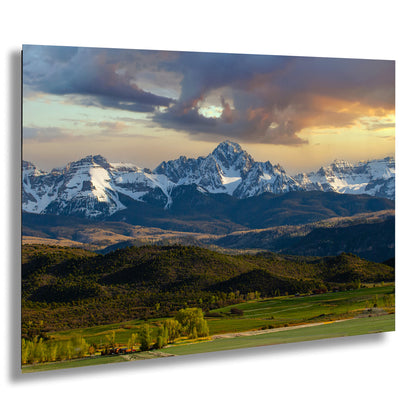 a breathtaking mountain range with snow-capped peaks against a vibrant sky, surrounded by lush green forests and rolling hills.