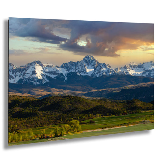 a breathtaking mountain range with snow-capped peaks against a vibrant sky, surrounded by lush green forests and rolling hills.