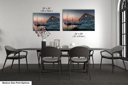 a dining room with a large dining table surrounded by six chairs. There is a vase of flowers on the table, and two framed prints of a building and a sailboat are displayed on the wall above the table.