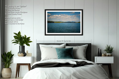 a serene bedroom scene with a large bed, nightstands, and a framed landscape photograph of a calm lake and blue sky above it.