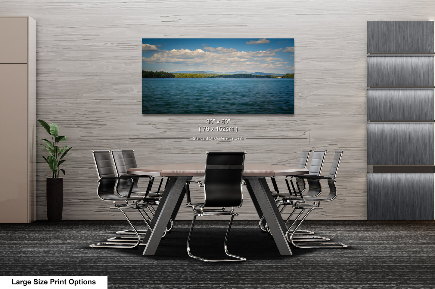 A modern office space with a large wooden table surrounded by black chairs, and a framed landscape photograph of a lake and mountains hanging on the wall above the table.