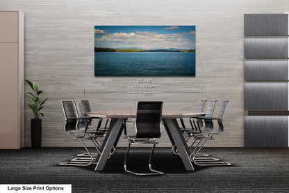 A modern office space with a large wooden table surrounded by black chairs, and a framed landscape photograph of a lake and mountains hanging on the wall above the table.