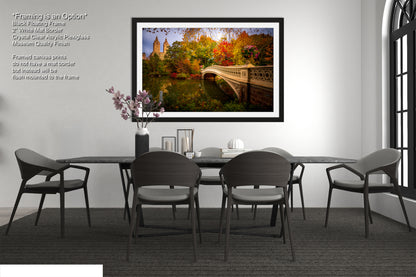 a bedroom with a large bed, a nightstand, and a framed picture of a bridge with autumn foliage.