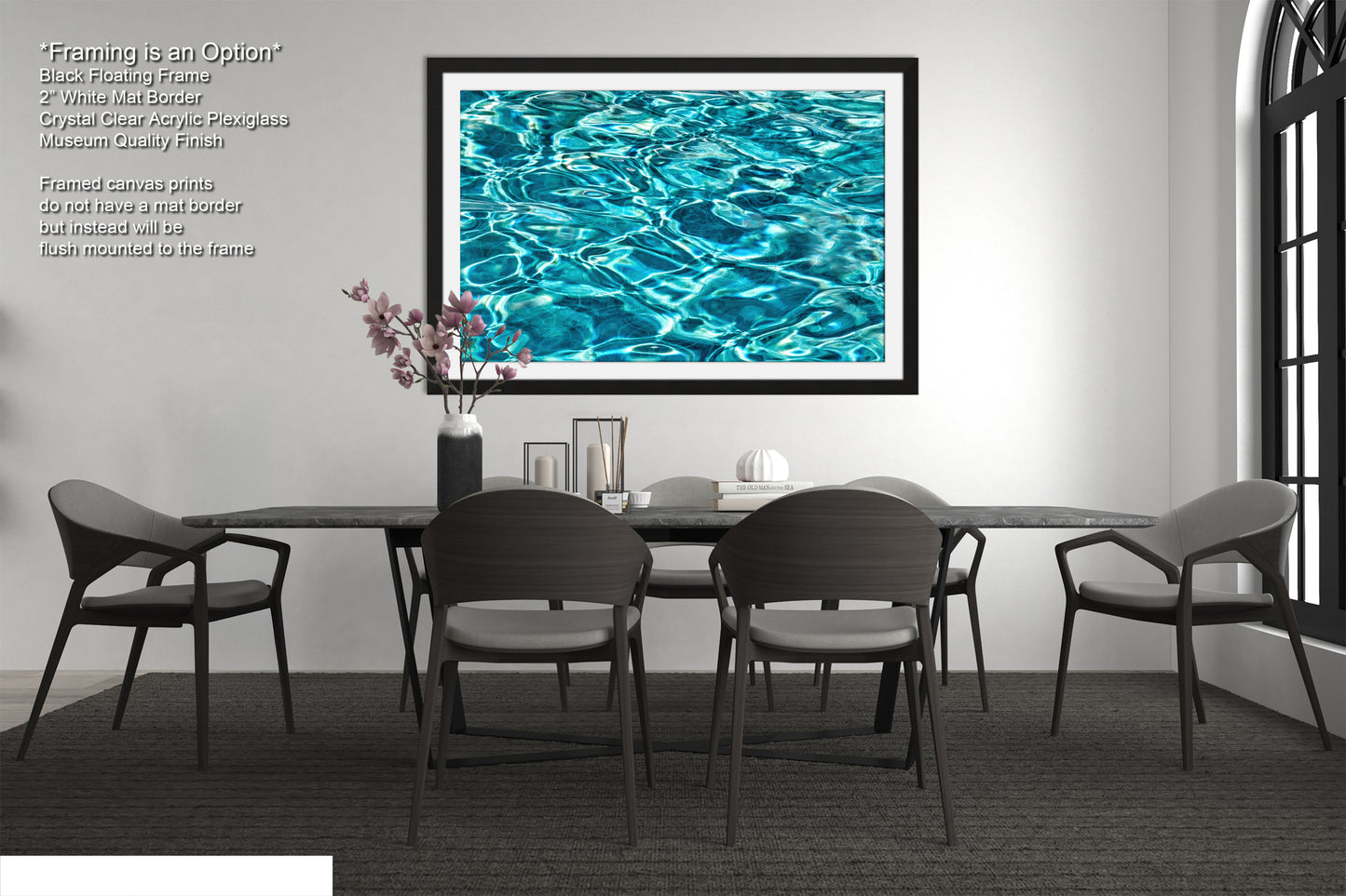 a modern dining room with a black table and chairs, a large framed picture of a blue water surface hanging on the wall, and a vase of pink flowers on the table.