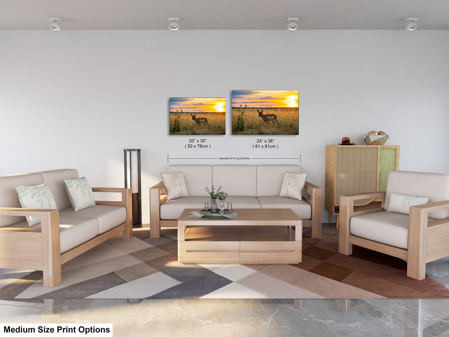 a modern living room with a white sofa, two chairs, and a coffee table. There are two framed landscape paintings on the wall, depicting a sunset over a field with a deer. The room has a neutral color scheme with a geometric patterned rug on the floor.