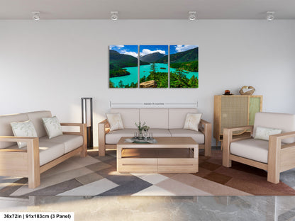The image is a modern living room with a large, three-panel landscape painting hanging on the wall. The painting depicts a scenic mountain landscape with a turquoise lake and lush green forests. The room is furnished with a sofa, two armchairs, and a coffee table, creating a comfortable and inviting atmosphere.