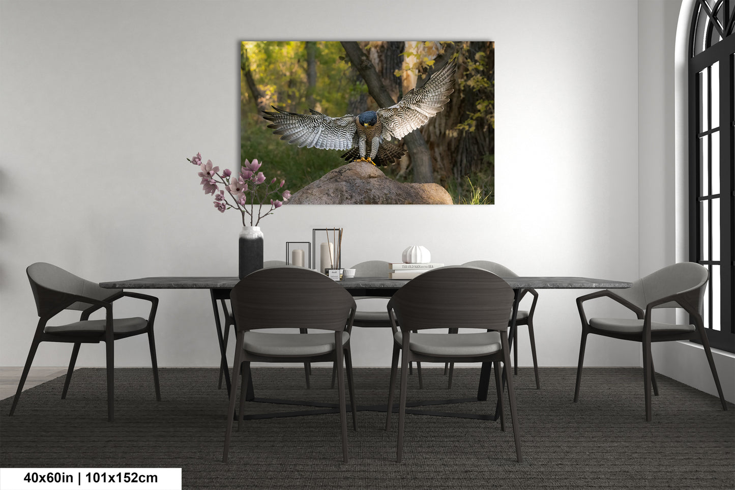 a large bird of prey, possibly a hawk or falcon, with its wings spread wide, perched on a rock in a forest setting. The bird is the focal point of the image, which is displayed on the wall above a dining table with four chairs.