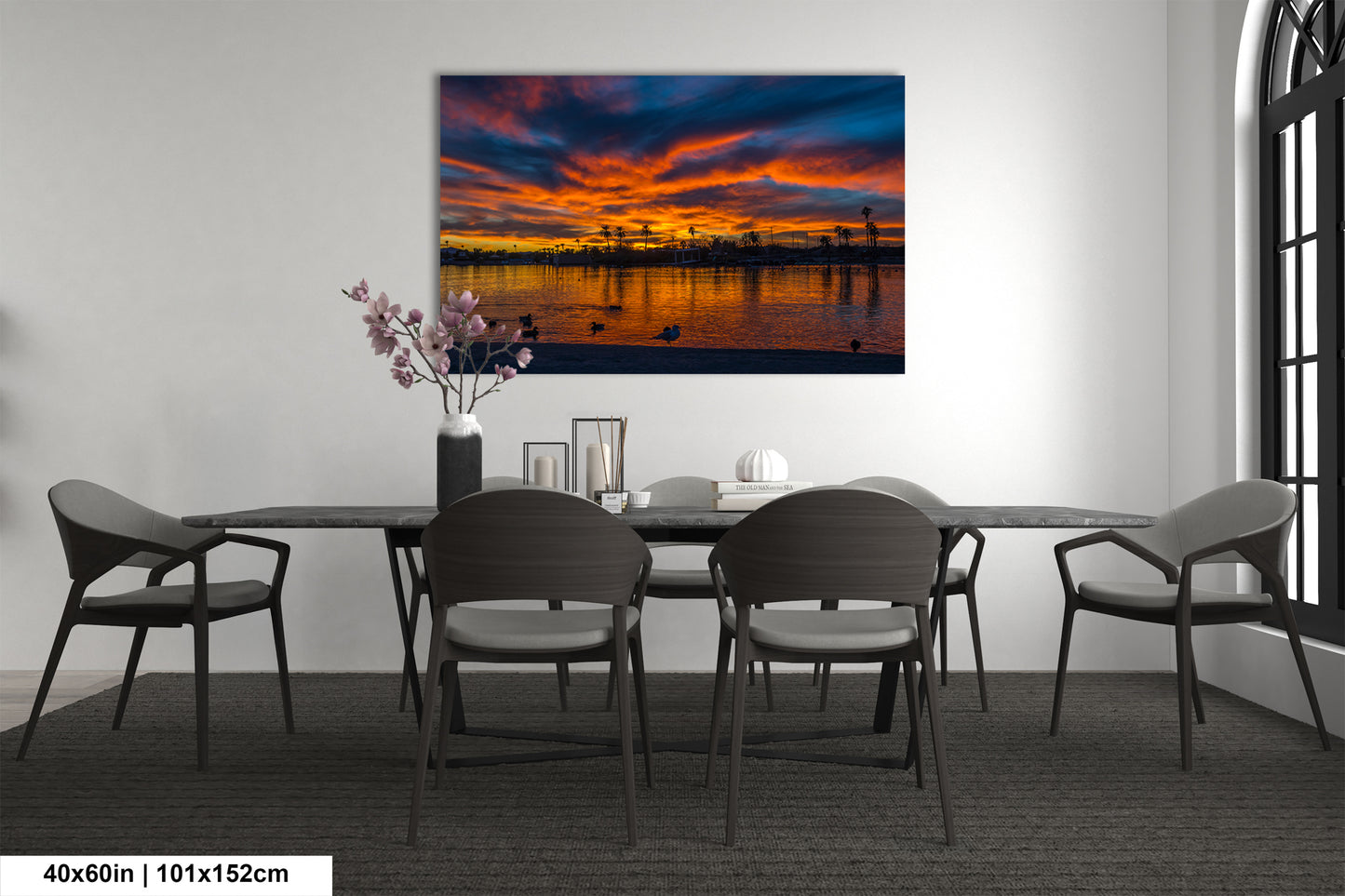 a dining room with a large painting of a sunset over a body of water hanging on the wall above a table with chairs.