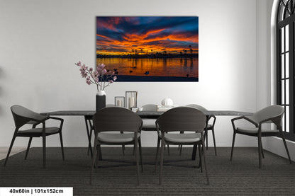 a dining room with a large painting of a sunset over a body of water hanging on the wall above a table with chairs.