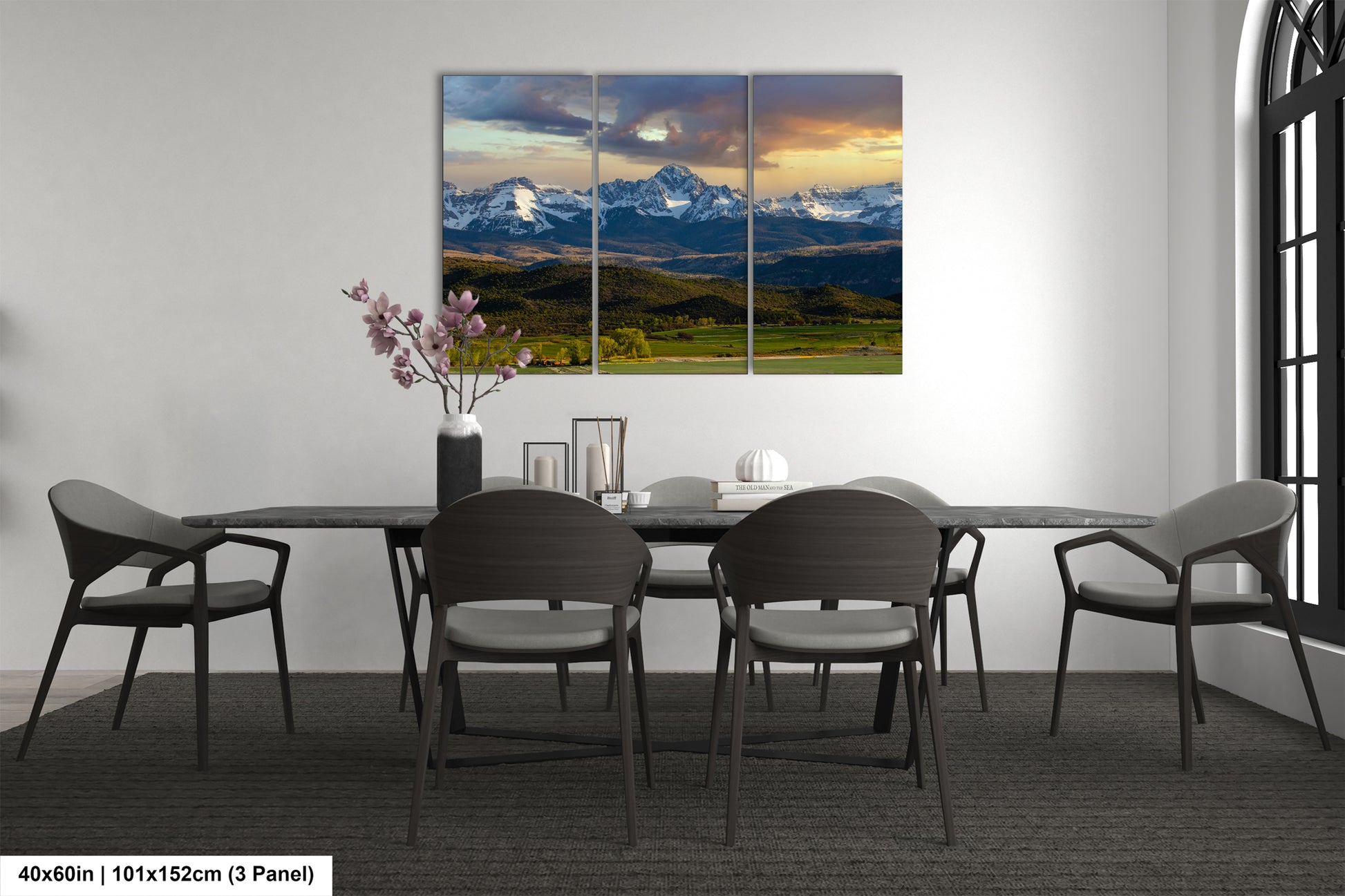 a modern dining room with a large, three-panel landscape painting of a mountain range hanging on the wall above a black dining table surrounded by six chairs.