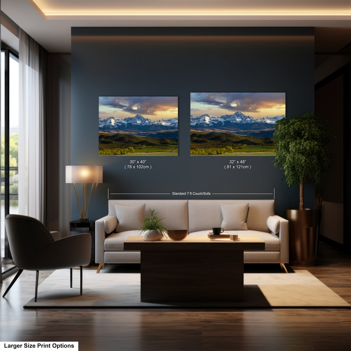 a modern living room with a large sofa, a coffee table, and a potted plant. The walls are painted in a dark color, and there are two framed landscape paintings hanging above the sofa. The paintings are of similar size and style, and the text indicates that the larger size print options are available.