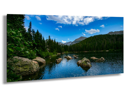 a serene lake surrounded by a forested mountain range, with a clear blue sky and fluffy white clouds above.