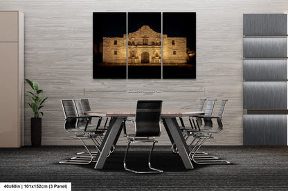 a modern office space with a large, illuminated photograph of the Alamo in the background. The photograph is displayed on a wall above a conference table, which is surrounded by chairs. The office has a minimalist and contemporary design, with gray walls and a gray carpeted floor.