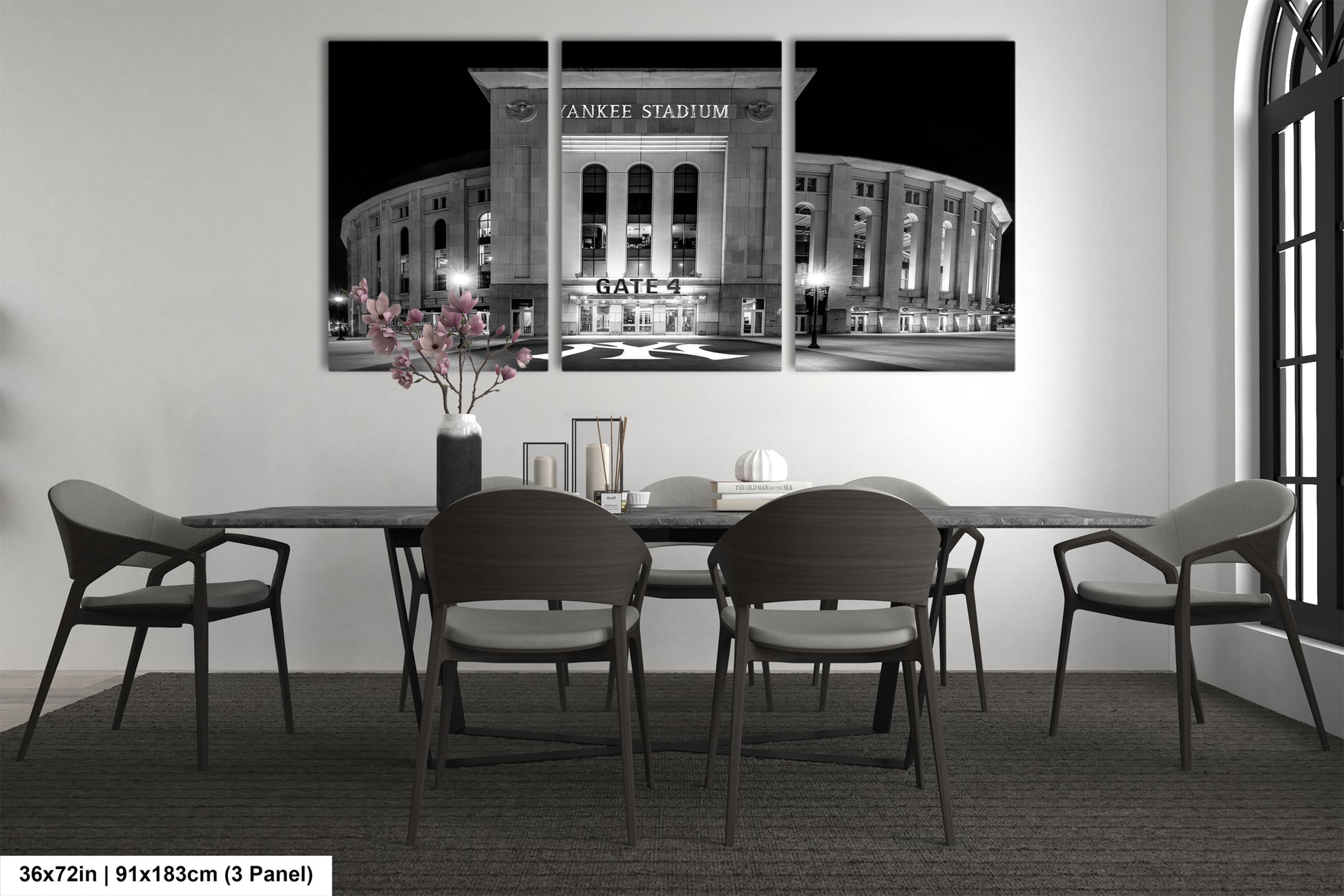 A black and white photograph of Yankee Stadium at night, with a vase of flowers on the table in front of it.