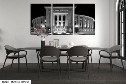 A black and white photograph of Yankee Stadium at night, with a vase of flowers on the table in front of it.