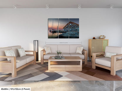 The image is a modern living room with a large, colorful painting of a boat on the wall. The room is furnished with a sofa, two chairs, and a coffee table. The painting is a collage of three panels, depicting a seascape with a building and boats in the background. The room has a minimalist and clean design, with white walls and a neutral color palette.