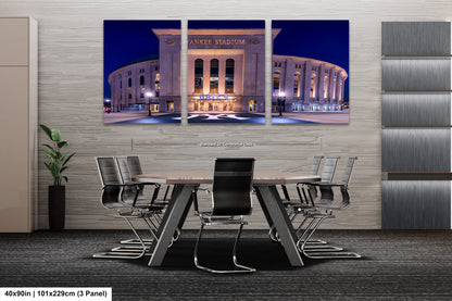 A modern office space with a large, illuminated image of Yankee Stadium in the background. The stadium is surrounded by a circular driveway and is illuminated at night, creating a striking visual effect. The office features a conference table with chairs, suggesting a professional setting.