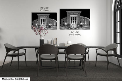 a dining room with a long table and four chairs. There are two framed black and white photographs of the Yankee Stadium, which is a baseball stadium located in New York City. The photographs are hung on the wall above the table, and the text indicates the size of the prints in inches.