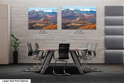 a modern office space with a large wooden table surrounded by black chairs. Two large landscape paintings are displayed on the wall above the table, depicting mountains and a desert scene.