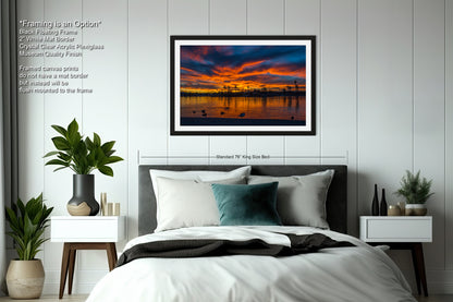 a bedroom with a large bed, nightstands, and a framed picture of a sunset over a body of water.