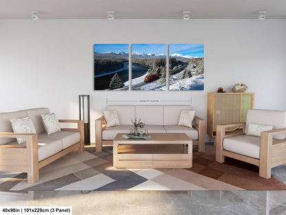 The image is a modern living room with a large, three-panel landscape painting hanging on the wall. The painting depicts a snowy mountain landscape with a train passing through the scene. The room is furnished with a sofa, two chairs, and a coffee table, creating a cozy and inviting atmosphere.
