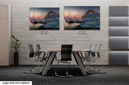 a modern office space with a large wooden table surrounded by black chairs. Two framed prints of a serene harbor scene are displayed on the wall above the table, creating a calming atmosphere.