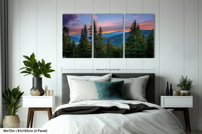 A bedroom with a large bed, nightstands, and a large wall art depicting a scenic mountain landscape with pine trees and a colorful sunset.