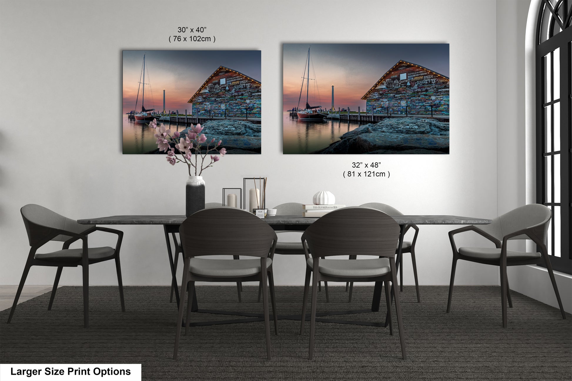 a dining room with a large dining table and six chairs. There are two framed paintings hanging on the wall above the table, depicting a serene harbor scene with a building and a boat. The paintings are of different sizes, with one being larger than the other.