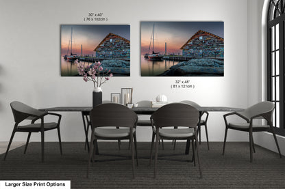 a dining room with a large dining table and six chairs. There are two framed paintings hanging on the wall above the table, depicting a serene harbor scene with a building and a boat. The paintings are of different sizes, with one being larger than the other.