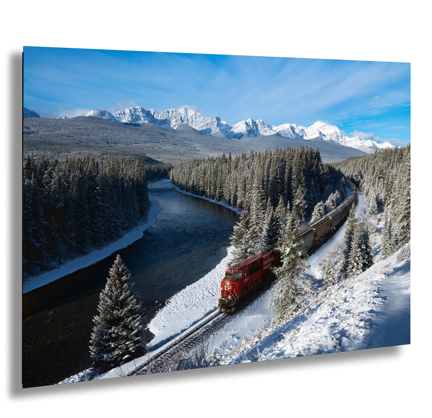 A red train travels along a snowy track through a picturesque winter landscape, with snow-covered mountains and trees in the background.