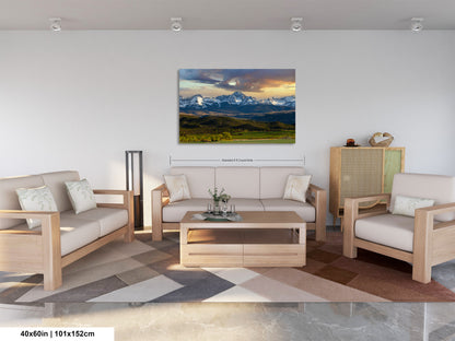 a living room with a large landscape painting hanging on the wall. The painting features a mountain range and a colorful sky. The room is furnished with a sofa, two armchairs, and a coffee table. The furniture appears to be made of wood and has a neutral color palette. The overall design of the room is modern and minimalist, with a focus on clean lines and a sense of spaciousness.