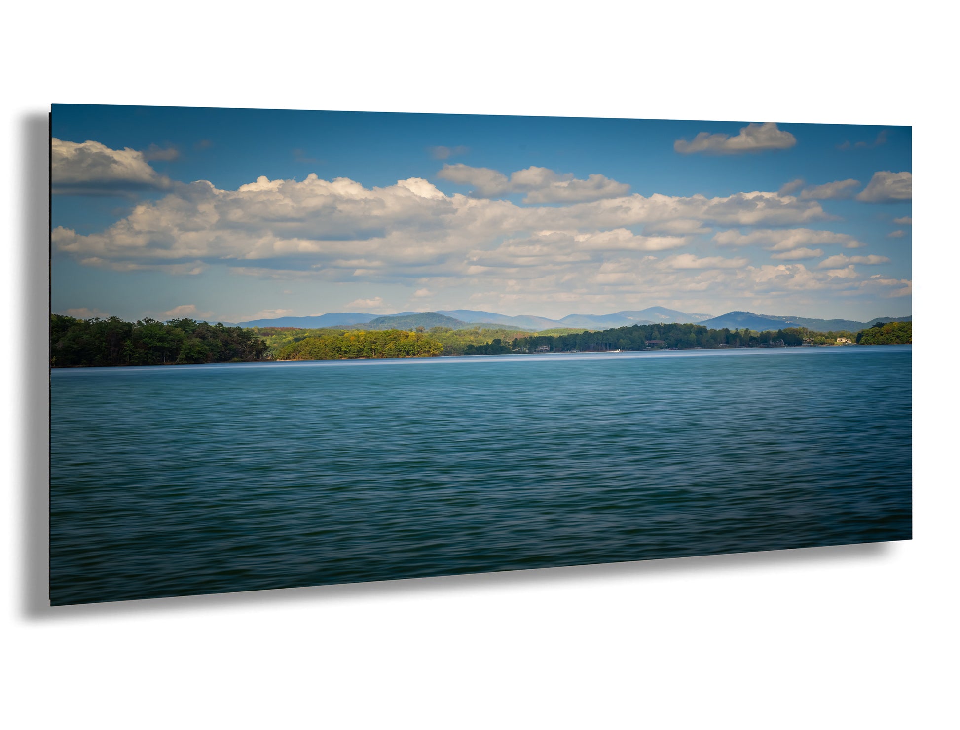 a serene lake surrounded by lush green trees and mountains under a blue sky with fluffy white clouds.