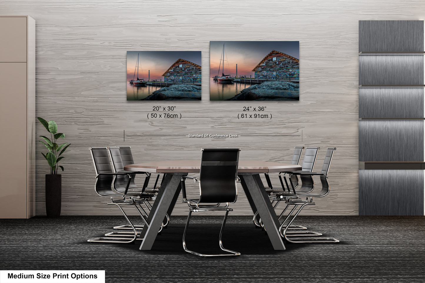 a modern office space with a large wooden table surrounded by black chairs. Above the table, there are two framed prints of a seascape, one depicting a sailboat and the other showing a building. The prints are of different sizes, with the larger one being 24" x 36" and the smaller one being 20" x 30". The prints are displayed on a wall, and there is a plant in the corner of the room.