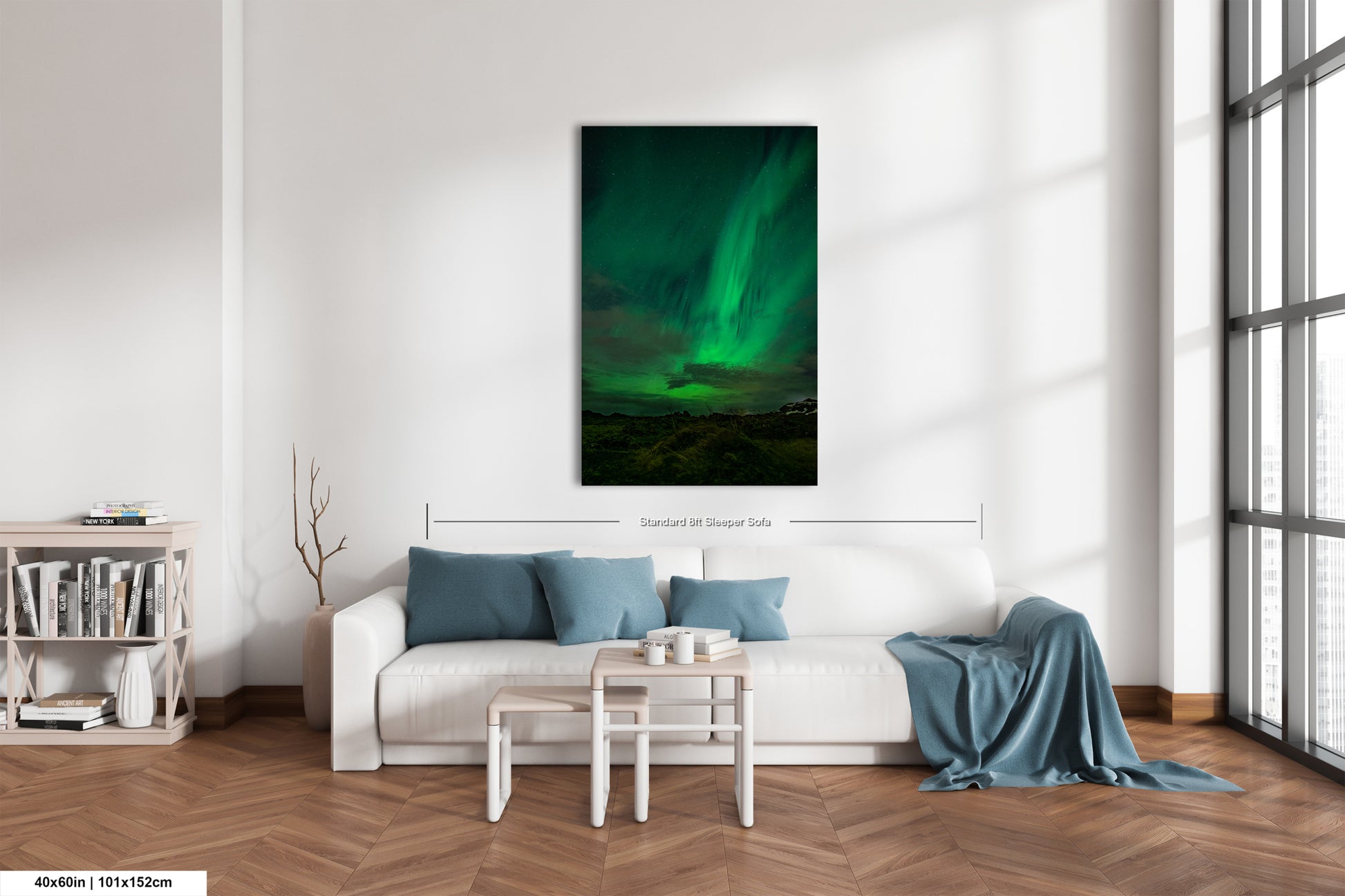 a living room with a white sofa, a coffee table, and a bookshelf. The room has a large window that allows natural light to enter, and a painting of the Aurora Borealis, or Northern Lights, is hanging on the wall.