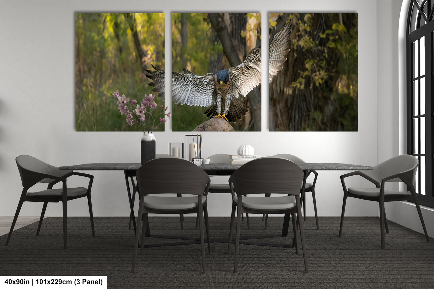 A modern dining room with a large wall-mounted painting depicting a bird of prey in flight. The painting is divided into three panels, with the central panel showing the bird in full flight. The dining table is surrounded by four chairs, and there are some decorative elements such as a vase and a book on the table.