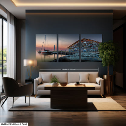 The image is a modern dining room with a large wall-mounted collage of three pictures depicting a serene harbor scene at sunset. The collage features a sailboat, a building with colorful graffiti, and a peaceful landscape with a body of water and a dock. The dining table is surrounded by four chairs, and the room has a minimalist and contemporary design with a neutral color palette.