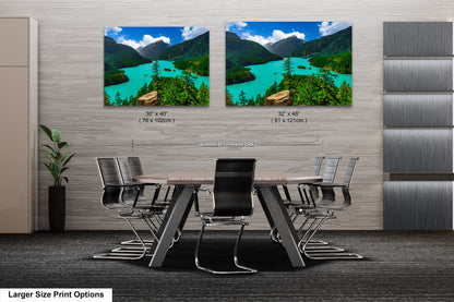 a modern office space with a large wooden table surrounded by black chairs. Two large landscape paintings are displayed on the wall above the table, depicting a scenic mountain view with a turquoise lake.