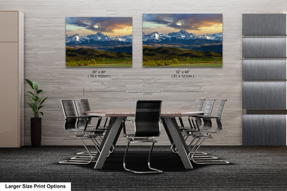 a modern office space with a large wooden table surrounded by black chairs. Two framed landscape paintings are displayed on the wall above the table, depicting a scenic mountain landscape.