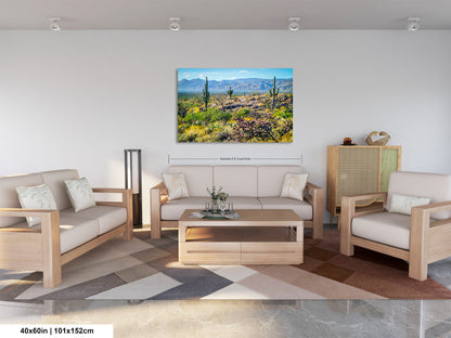 a living room with a large, colorful painting of a desert landscape hanging on the wall. The painting features a desert scene with cacti, mountains, and a clear blue sky. The living room is furnished with a sofa, two chairs, and a coffee table, creating a cozy and inviting atmosphere.